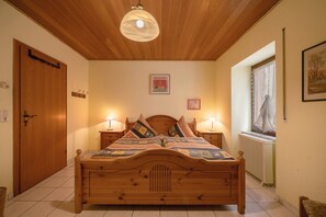 Un lit en bois avec une tête de lit, deux tables de chevet avec des lampes, une fenêtre avec des rideaux, un radiateur et une porte en bois.