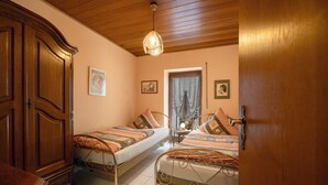 A bedroom with two single beds, a wooden wardrobe, a ceiling light, and a window with curtains.