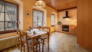 A dining area with a table set for four, wooden chairs, a chandelier, and a kitchen with a stove and oven.