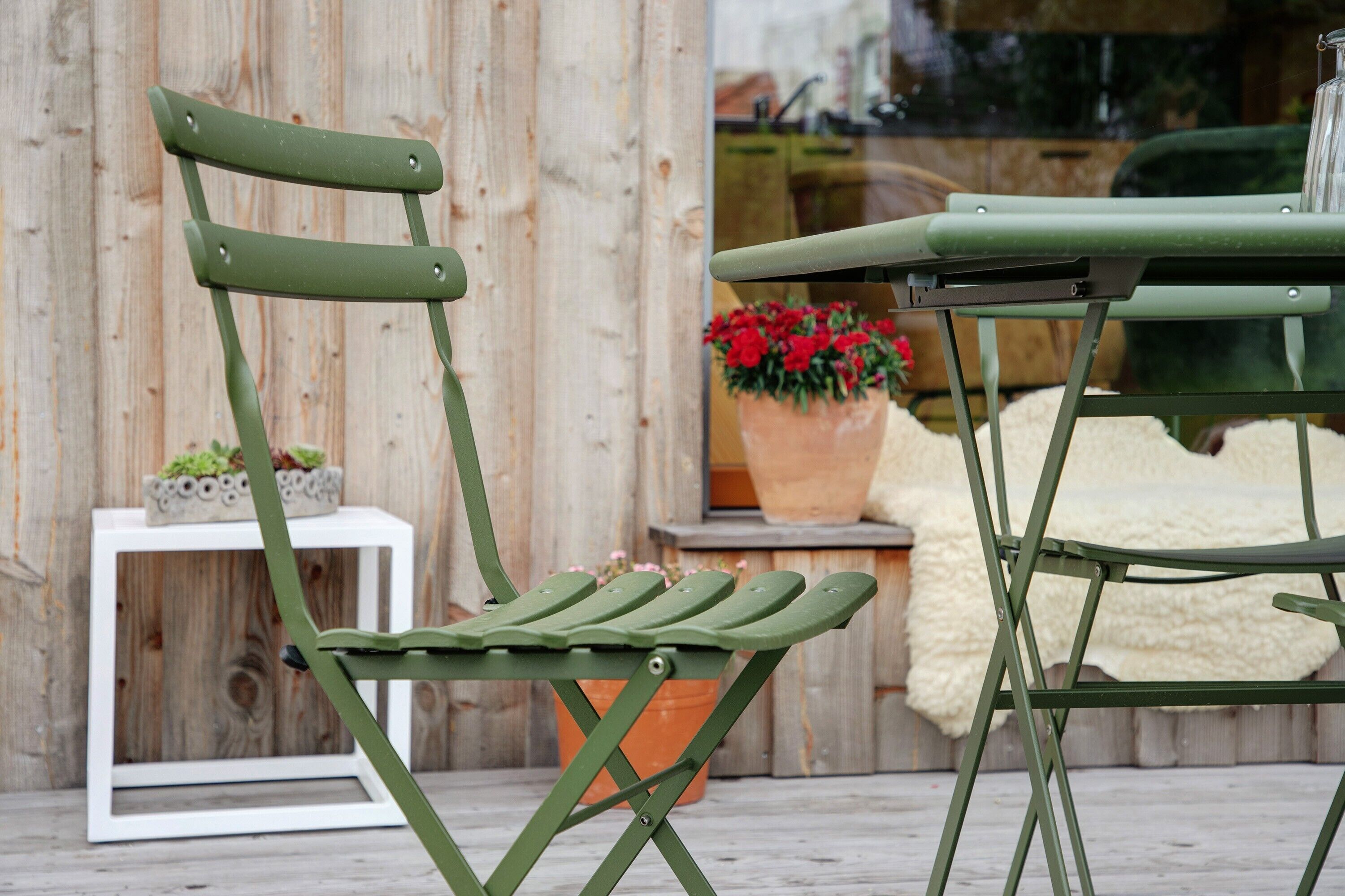 A green chair with a white table and a potted plant in the background.
