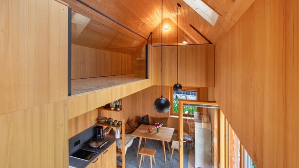 Interior compacto de madera con cama en literas, kitchenette, comedor y escalera.