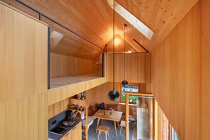 A compact, wooden interior with a loft bed, kitchenette, dining area, and a staircase.