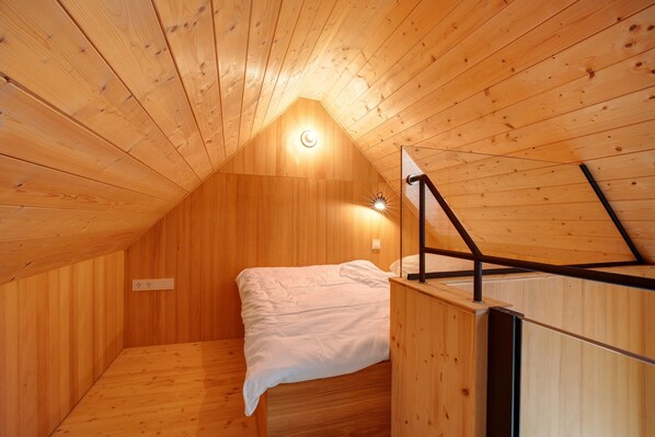 A small, wooden-paneled attic bedroom with a single bed, a slanted ceiling, and a light fixture.