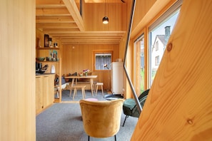 A wooden interior with a dining area, kitchen, and large windows.