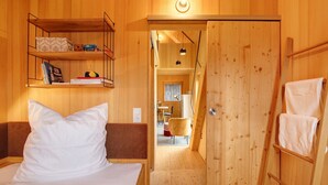 Una habitación de madera con una cama, una estantería llena de libros, una silla y un armario de madera.