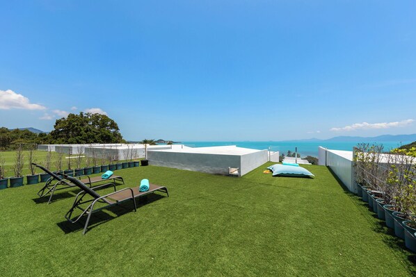 Una terraza en la azotea con césped artificial, sillas de descanso y vista al mar.