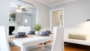 Ein Essbereich mit einem weißen Tisch, Stühlen, einer Chandelier und einer Couch.