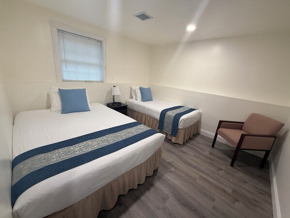 A hotel room with two beds, a chair, a window, and a nightstand.