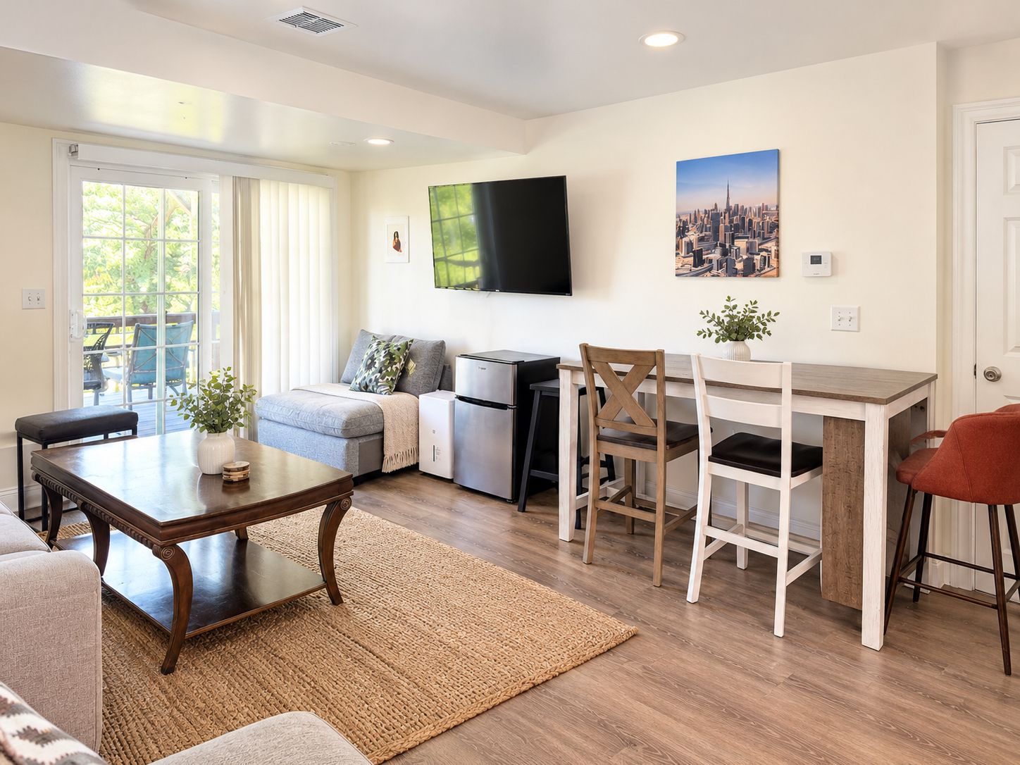A modern living room with a sofa, a dining table, and a TV mounted on the wall.