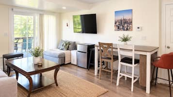 A modern living room with a sofa, a dining table, and a TV mounted on the wall.