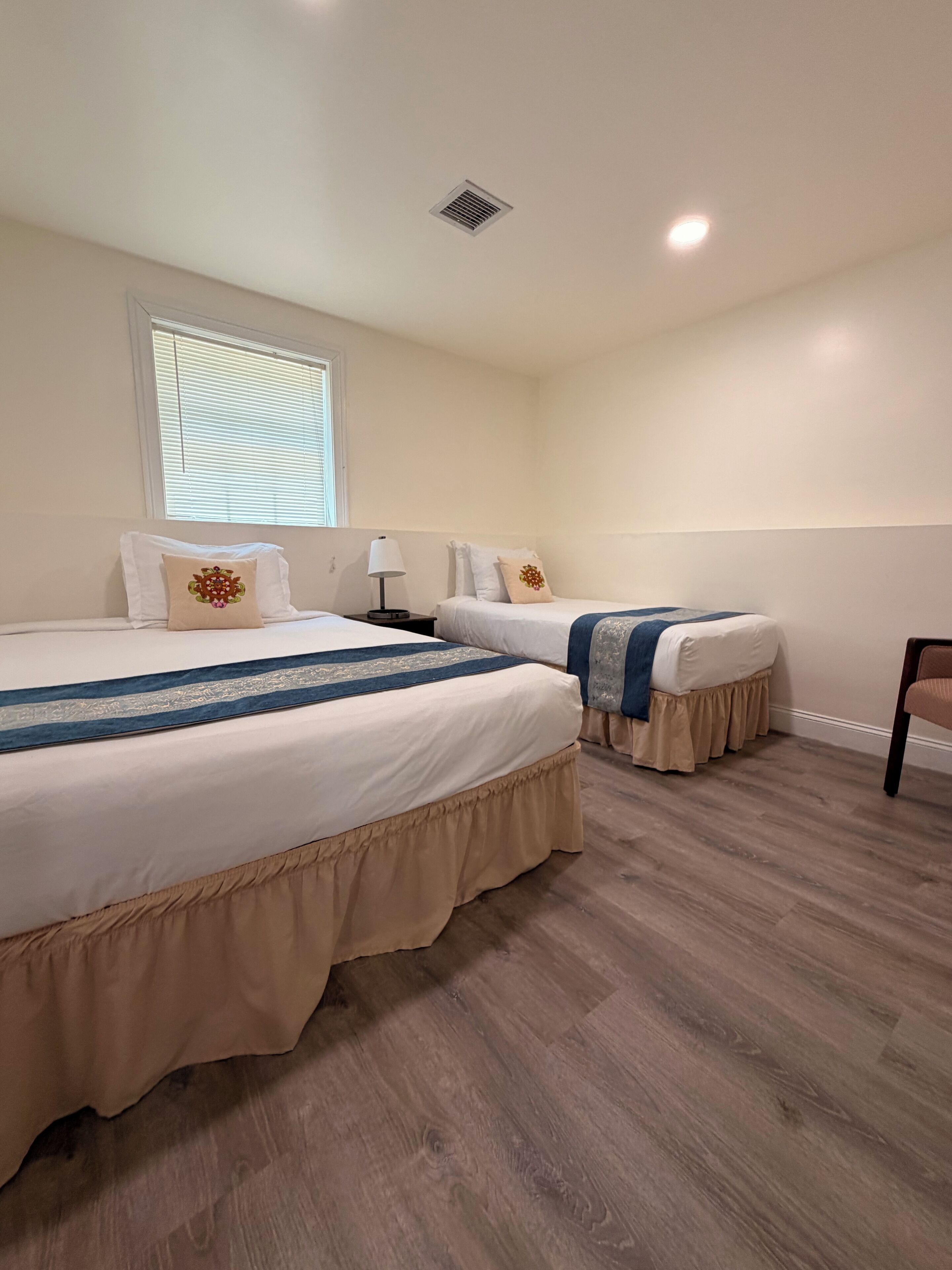 Habitación de hotel con dos camas, una ventana con persianas, una lámpara y una silla.