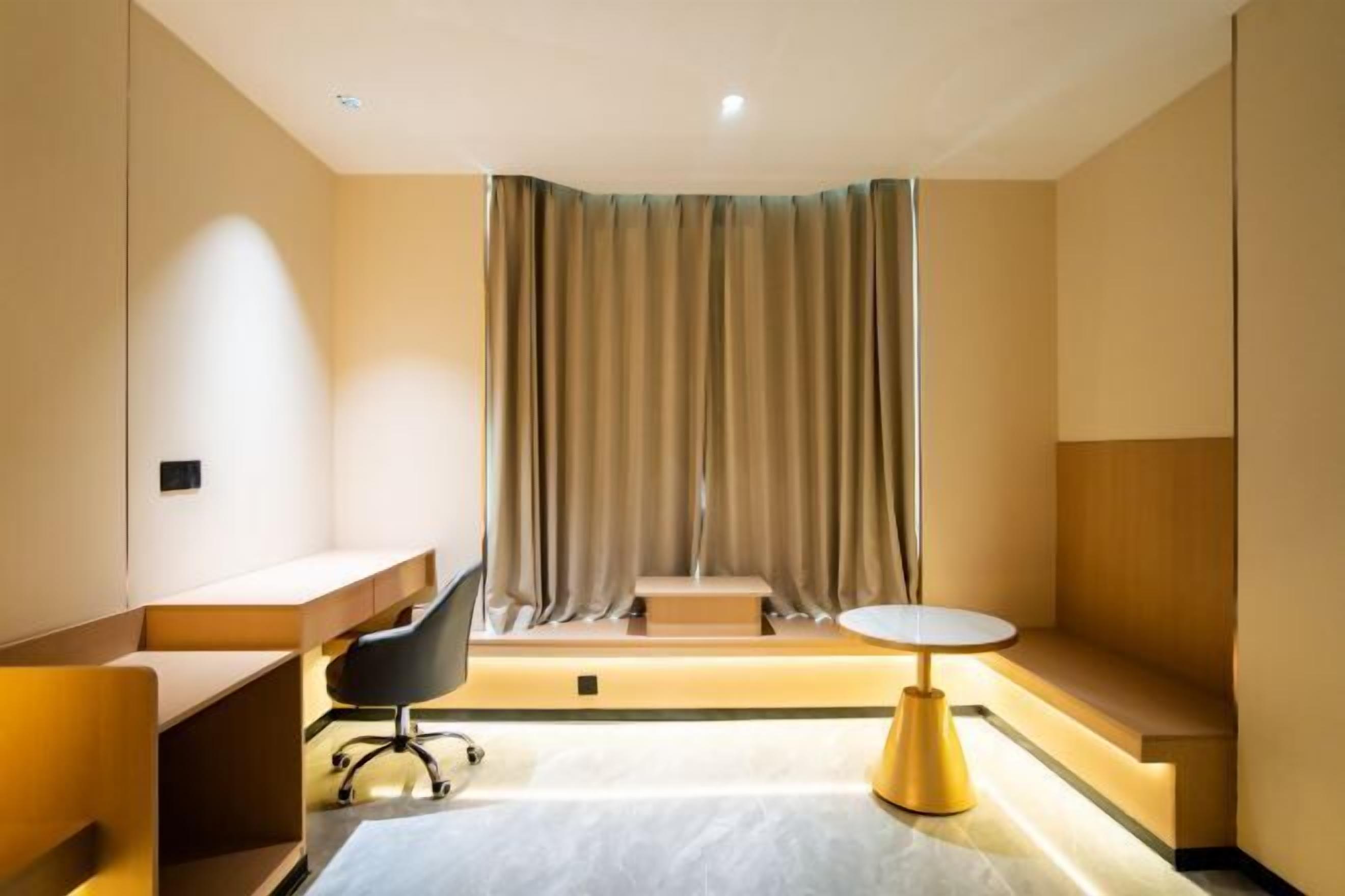 A modern hotel room with a desk, a chair, a small table, and a bench.