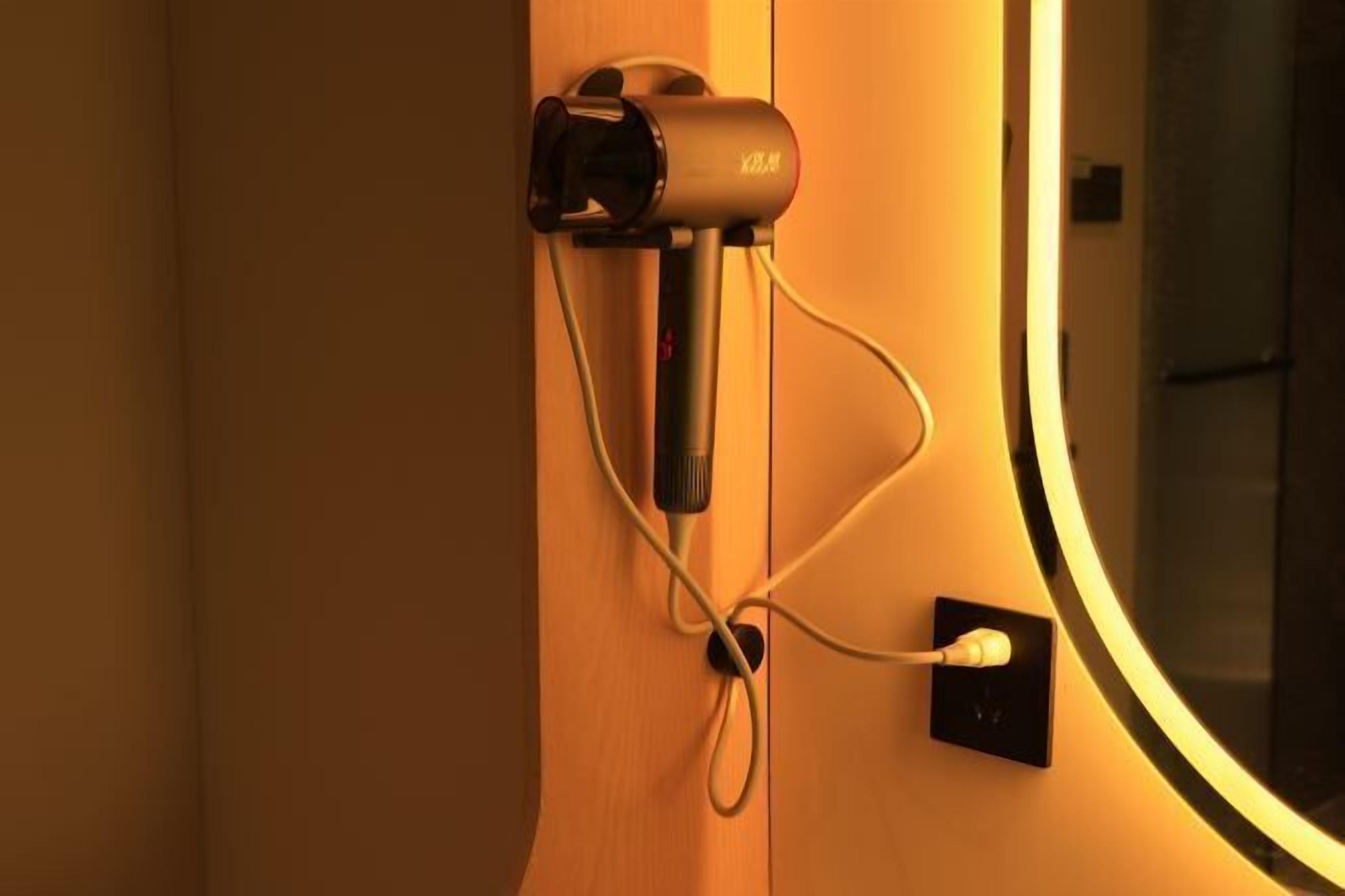 Eine an der Wand befestigte Vorrichtung mit Kabel, das in eine Steckdose gesteckt ist und mit einer runden Leuchte verbunden ist.