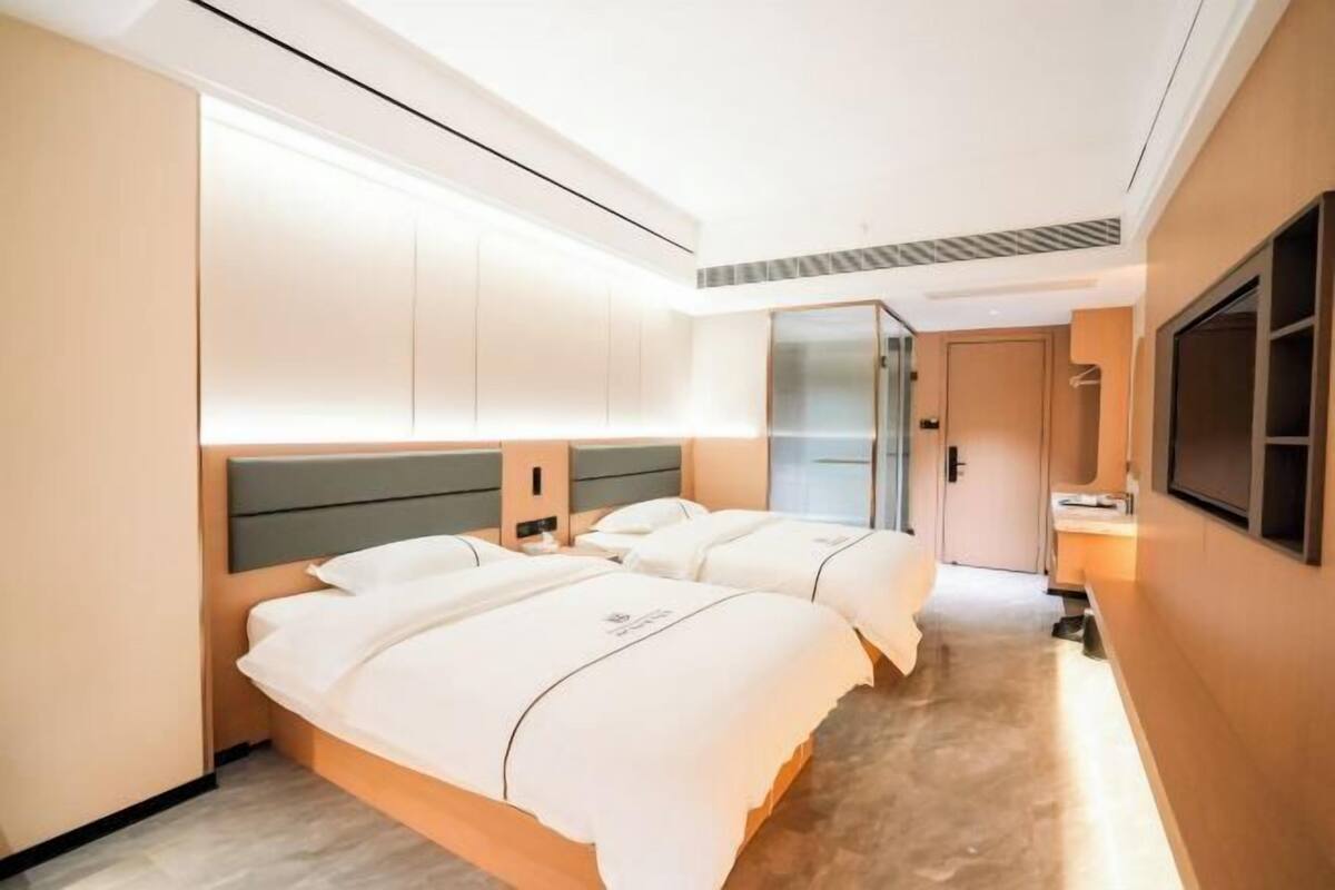 Ein Hotelzimmer mit zwei Betten, einem großen Spiegel und einem an der Wand befestigten Fernseher.
