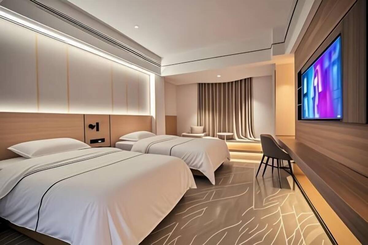 Ein modernes Hotelzimmer mit zwei Betten, einem Flachbildfernseher und einer Sitzecke mit Tisch und Stühlen.