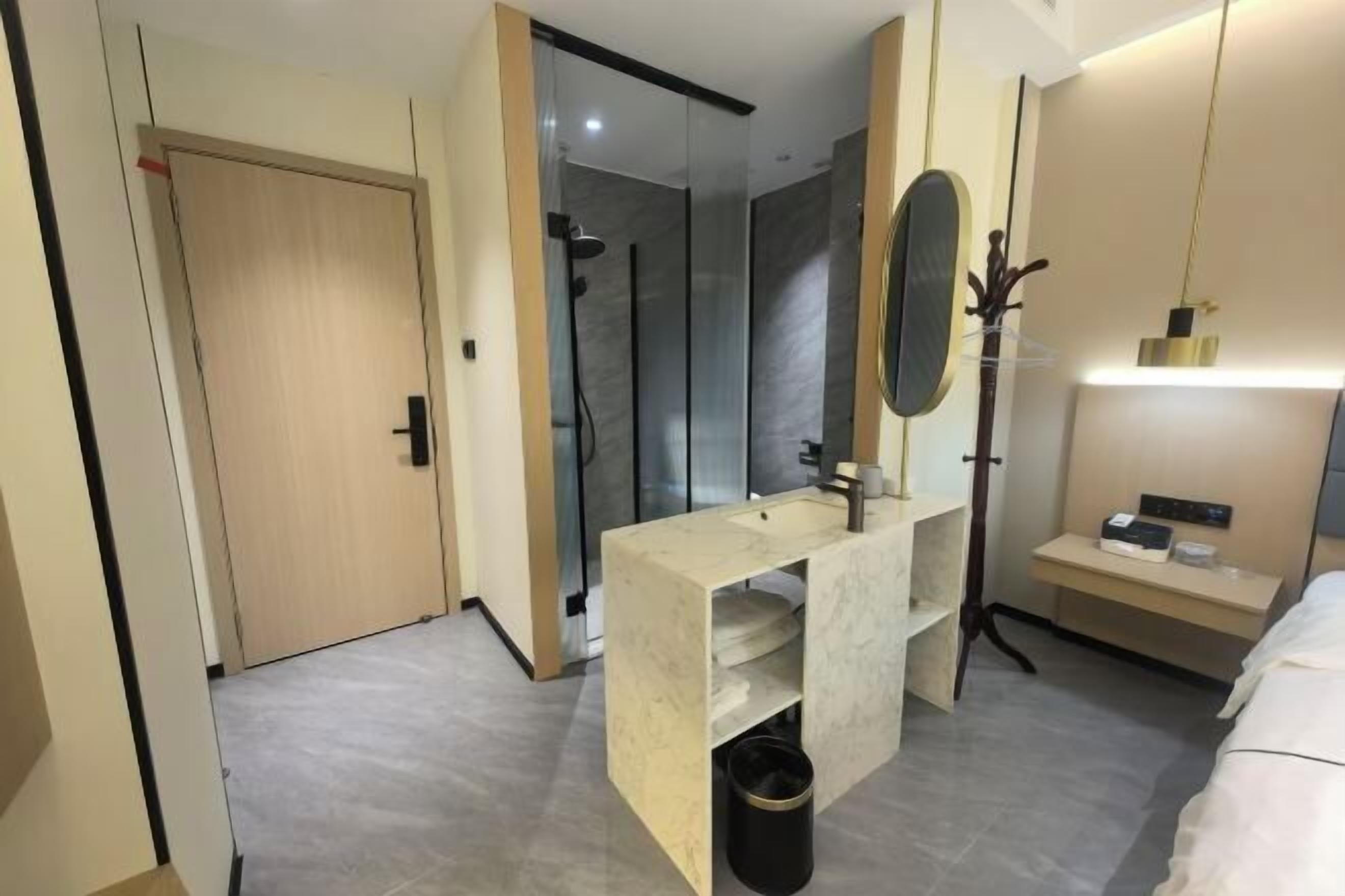 Une chambre d’hôtel moderne dotée d’un grand miroir, d’un lavabo intégré, d’un espace douche et d’une table de chevet avec une lampe.