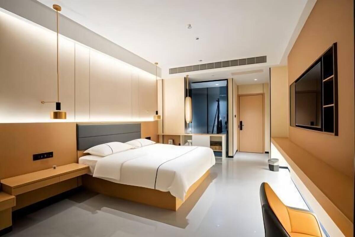Ein modernes Hotelzimmer mit einem Bett, Nachttischen, einem Fernseher und einem durch eine geöffnete Tür einsehbaren Badezimmer.