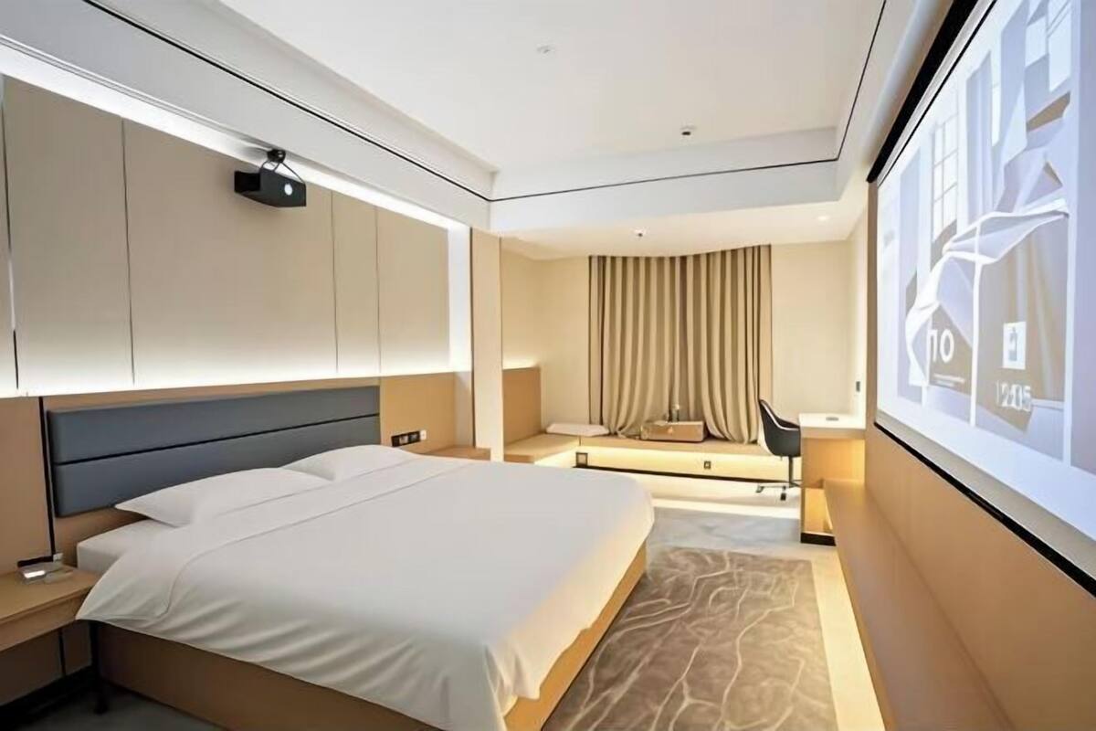 Ein modernes Hotelzimmer mit einem großen Bett, einem Schreibtisch, einem Stuhl und einem großen Fenster mit Blick auf die Stadt.