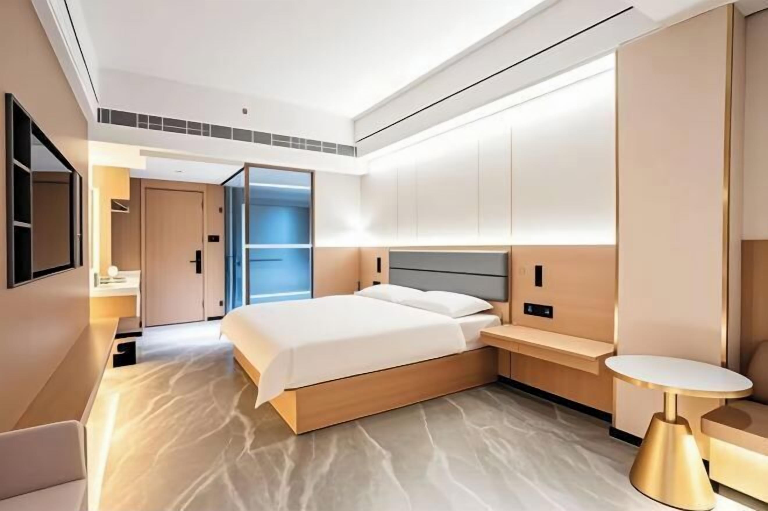 A modern hotel room with a large bed, built-in bedside tables, and a small round table.