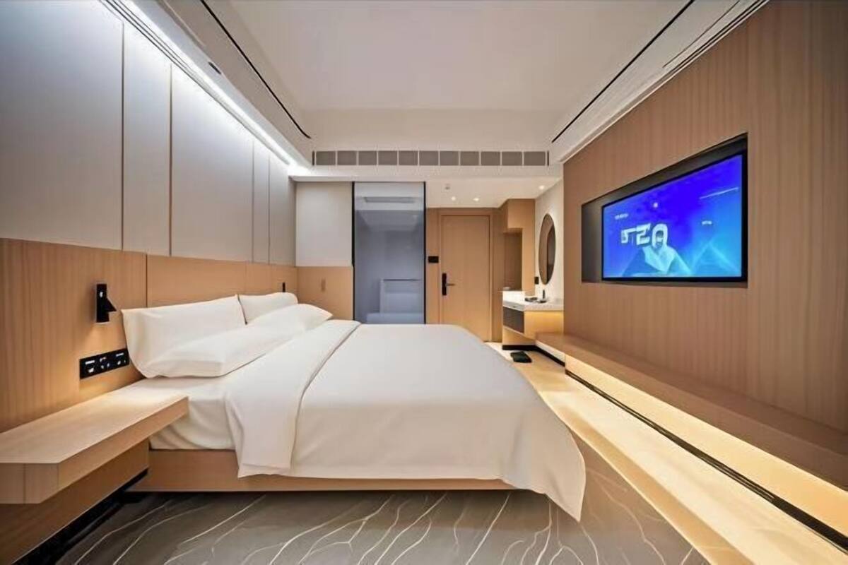 Ein modernes Hotelzimmer mit einem großen Bett, einem an der Wand montierten Fernseher und einem kleinen Nachttisch.