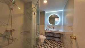 A bathroom with a glass-enclosed shower, a marble-tiled floor, a sink, and a mirror with a circular frame. - Viva Lavida Hotel (Bangkok)