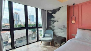 A hotel room with a large window, a bed, a chair, and a nightstand. - Viva Lavida Hotel (Bangkok)
