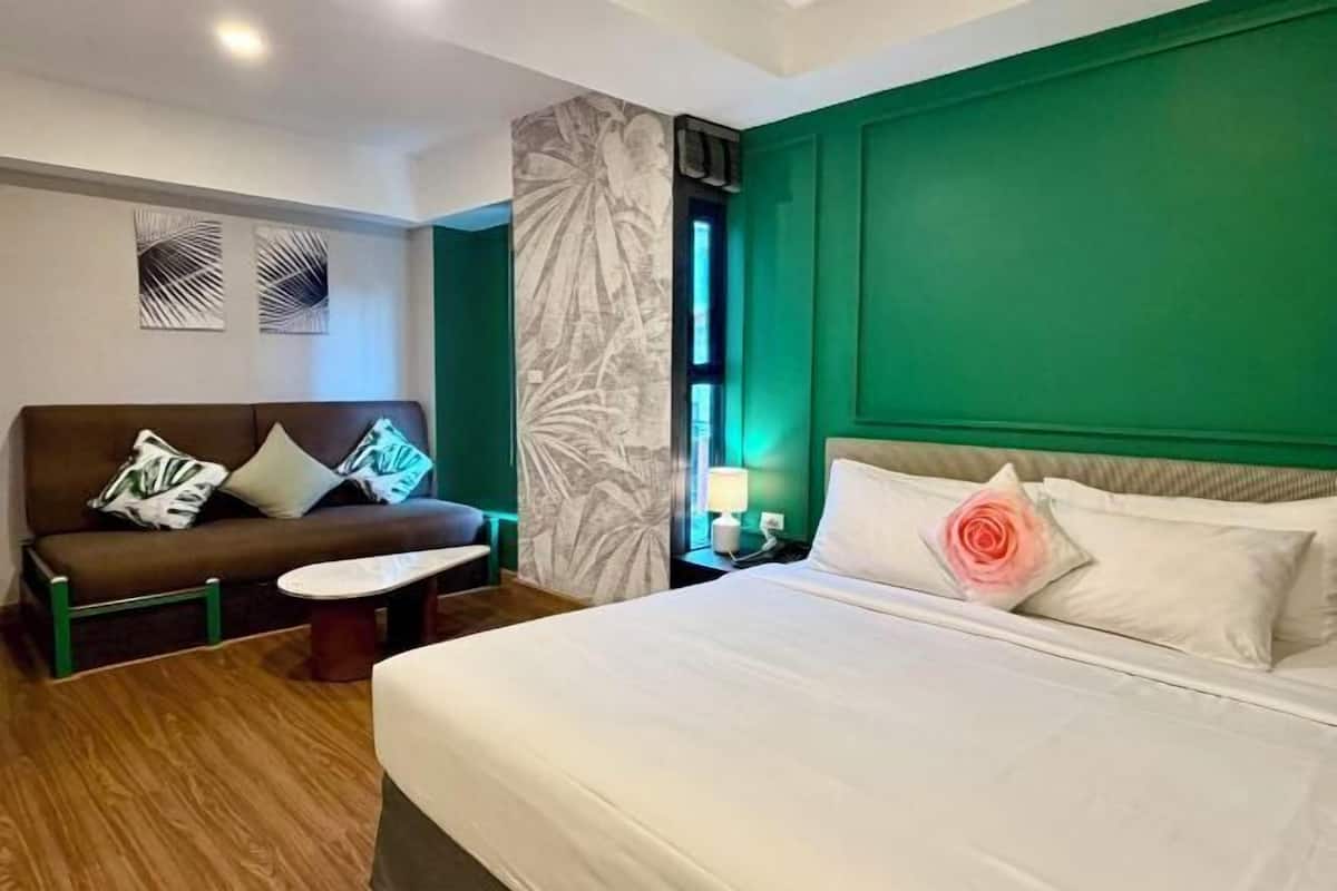 A hotel room with a bed, a sofa, a small table, and a nightstand with a lamp.