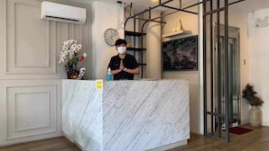 A reception area with a marble counter, a clock, and a person standing behind it. - Viva Lavida Hotel (Bangkok)