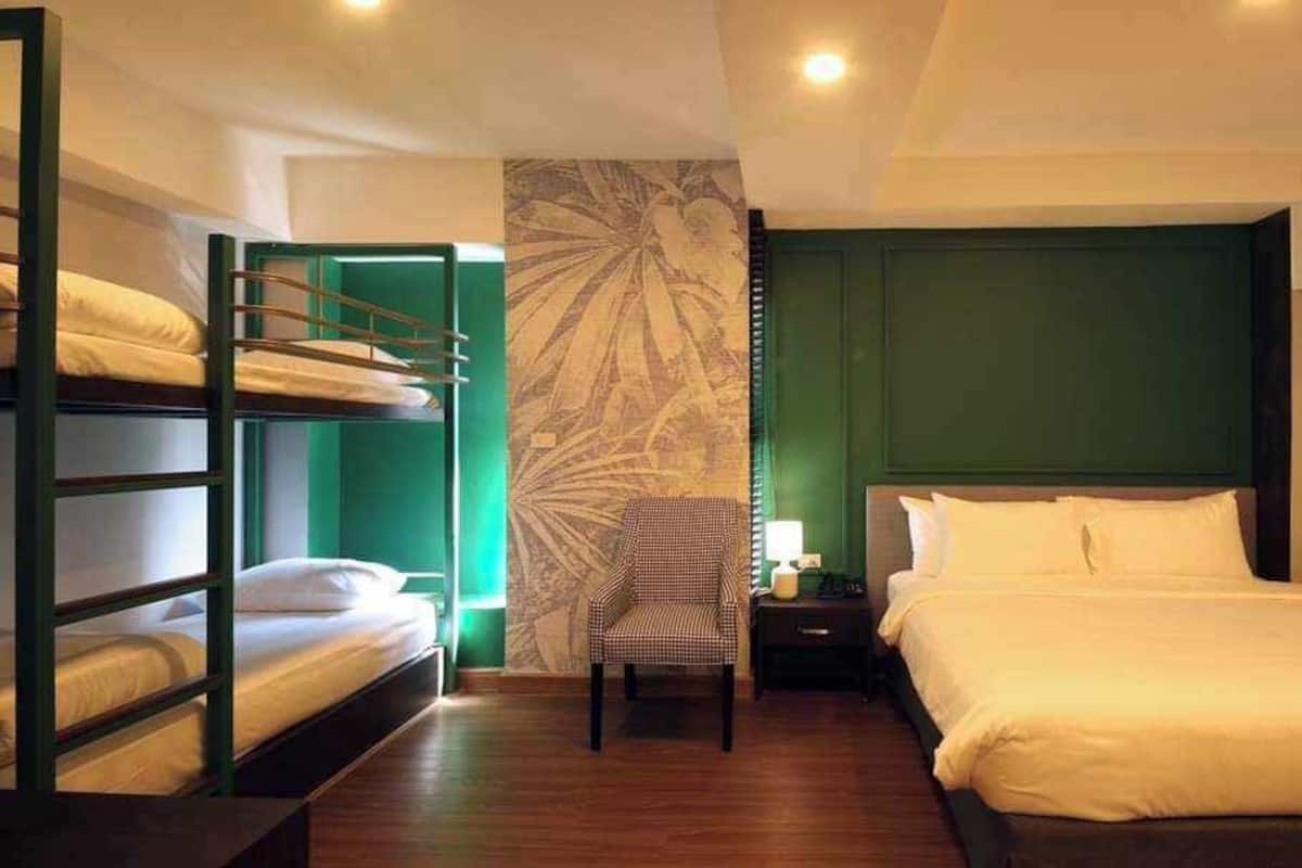 A hotel room with bunk beds, a single bed, a chair, a nightstand, and a green accent wall.