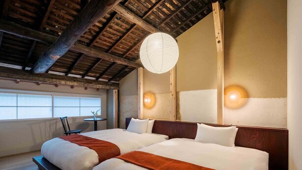 A hotel room with two beds, wooden beams on the ceiling, a large mirror, and two wall-mounted lights. - Akeiro Machiya House (Kyoto)