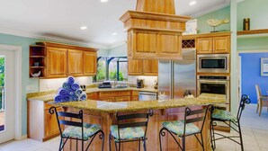 A kitchen with wooden cabinets, a granite countertop, a central island with chairs, and a stainless steel range hood. - Gorgeous 5 Bedroom Home with Heated Pool and Spa (Sanibel)