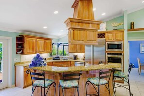 A kitchen with wooden cabinets, a granite countertop, a central island with chairs, and a stainless steel range hood.