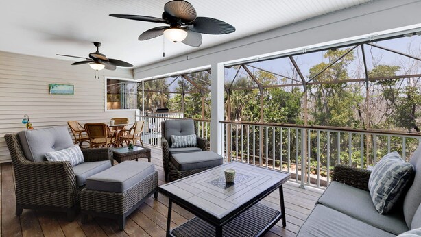 A covered outdoor area with wicker furniture, ceiling fans, and large windows. - Gorgeous 5 Bedroom Home with Heated Pool and Spa (Sanibel)