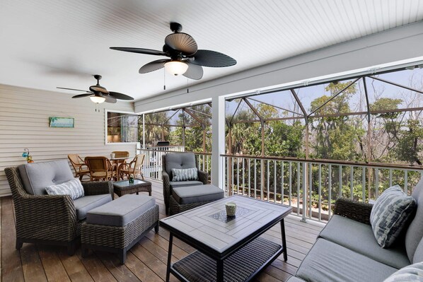 A covered outdoor area with wicker furniture, ceiling fans, and large windows.