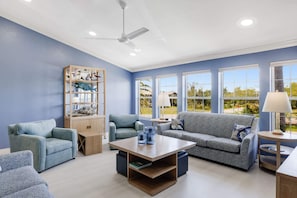 Un salon avec un mur bleu, un ventilateur de plafond, une table basse en bois, un canapé et une bibliothèque.