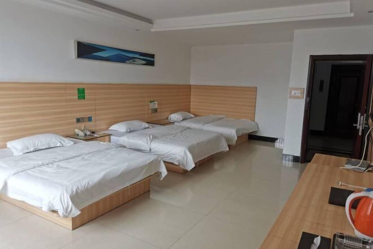 A hotel room with three beds, a wooden headboard, a desk with a chair, and a painting on the wall.