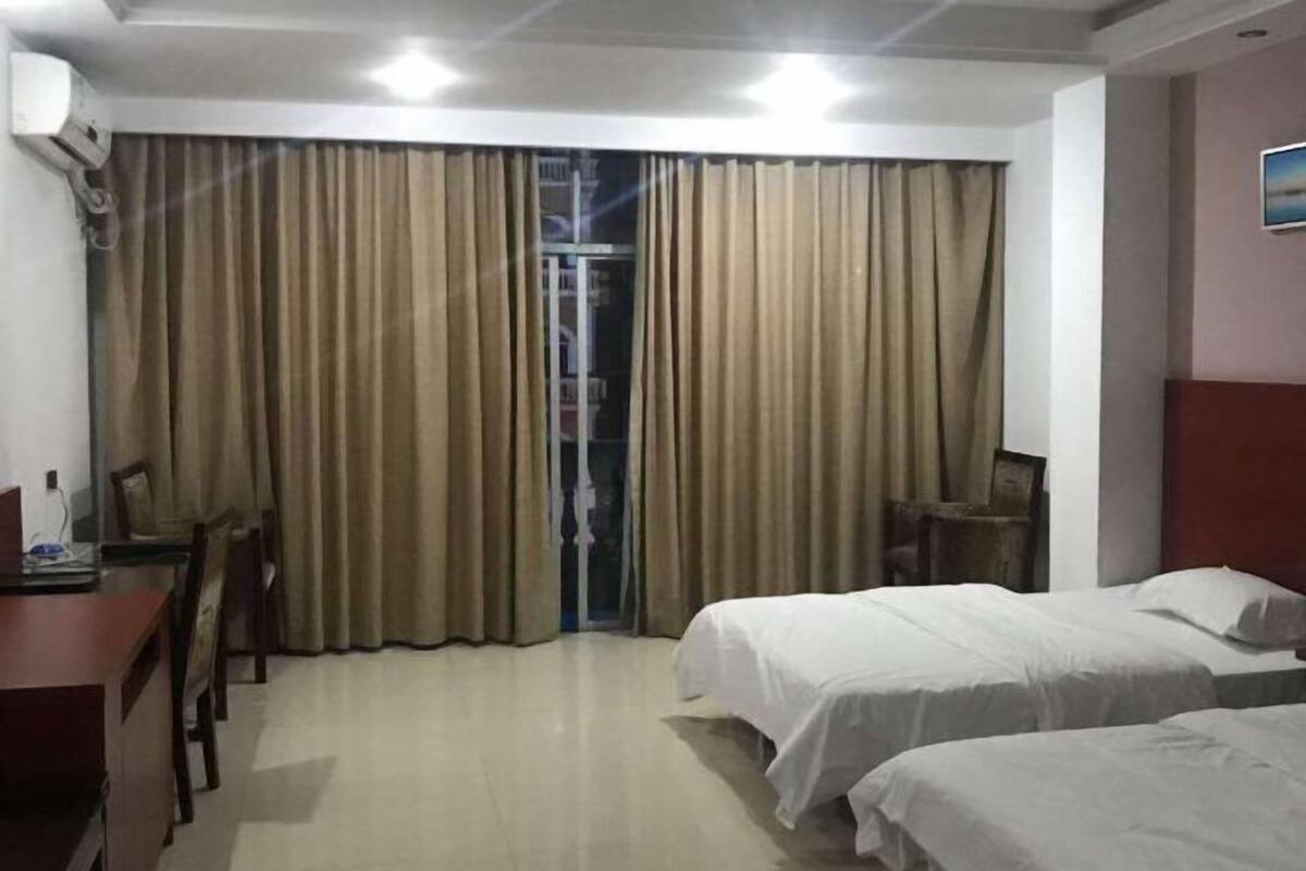 A hotel room with two beds, a desk, a chair, and a window with curtains.