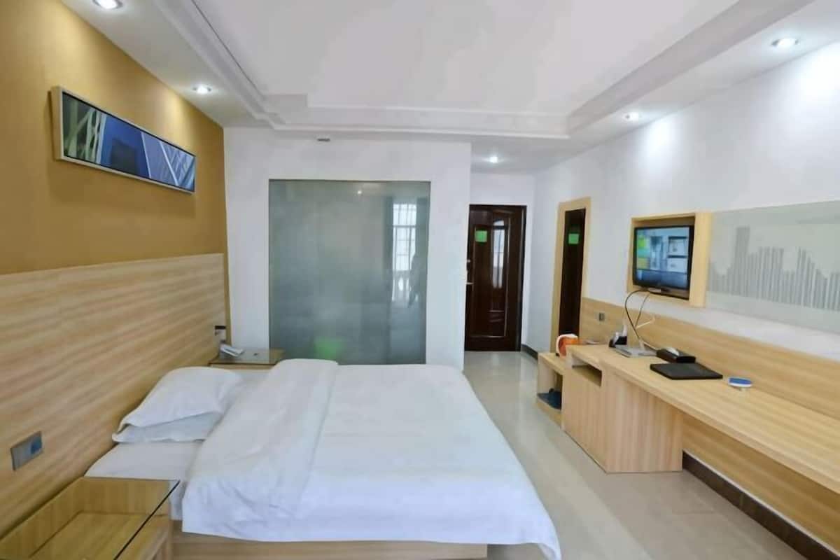A hotel room with a bed, a desk, a chair, a TV, and a door.