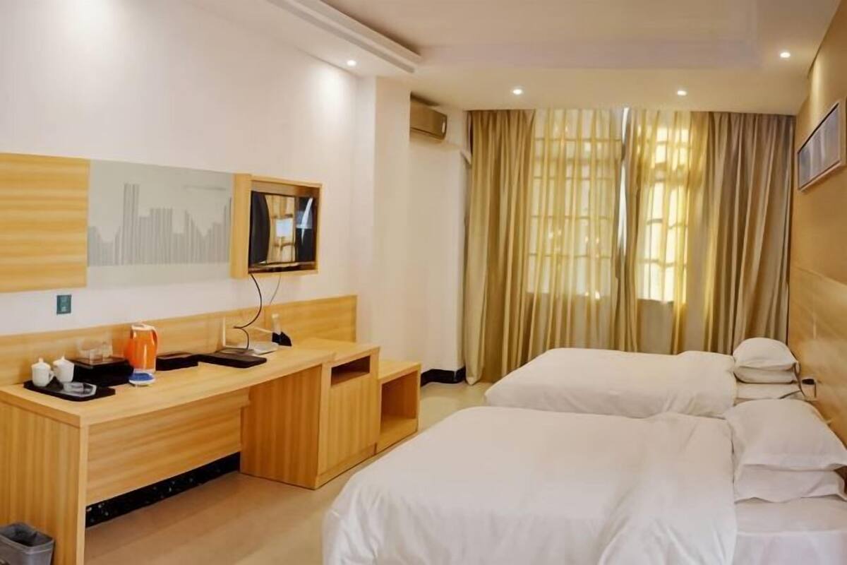 A hotel room with a wooden desk, two beds, a window with curtains, and a cityscape mural on the wall.