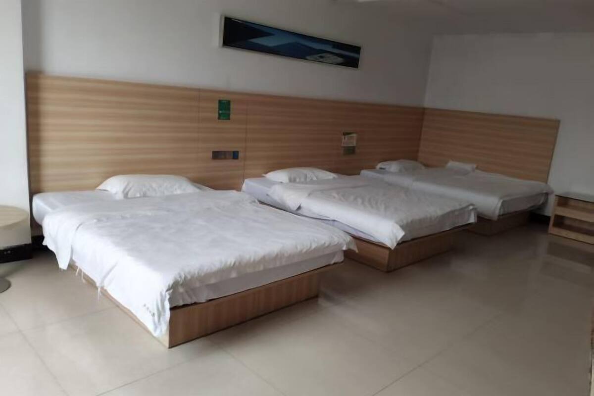 A hotel room with three single beds, a wooden headboard, a small bedside table, and a wall-mounted light.