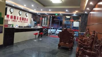 A hotel reception area with a reception desk, chairs, and a red carpet leading to the entrance.