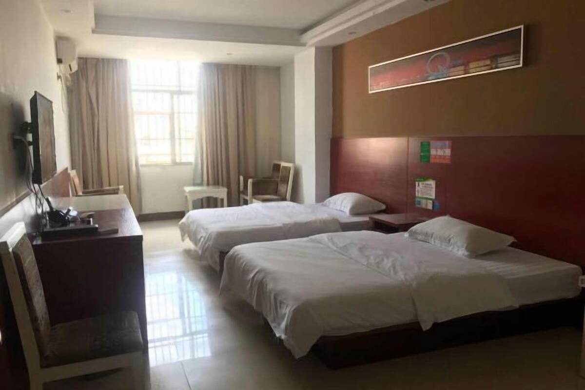 A hotel room with two beds, a desk with a chair, a TV, and a window with curtains.