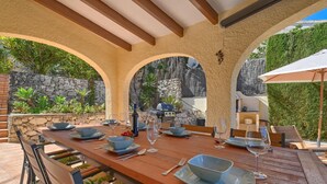An outdoor dining area with a stone wall, wooden table, and chairs.