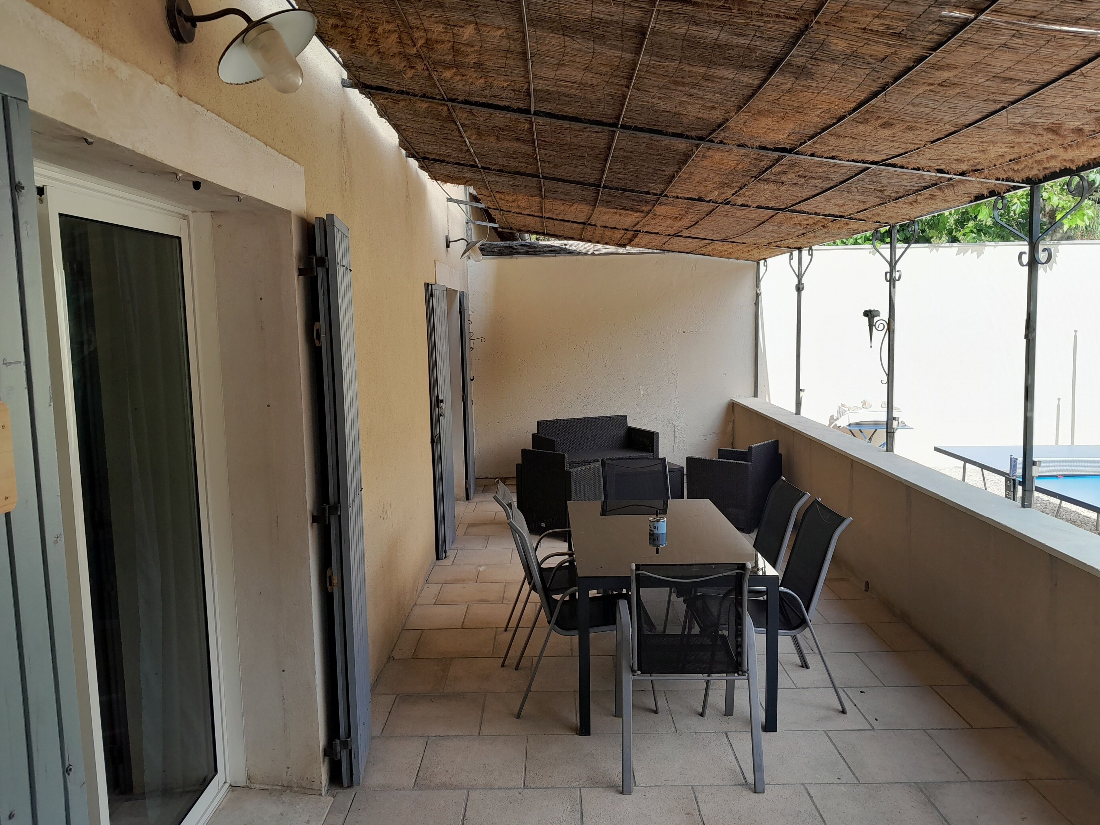 A covered outdoor seating area with a table and chairs, a door, and a view of a pool.