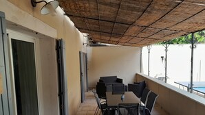 Un espacio de estar al aire libre techado con una mesa, sillas, una puerta y vista a una piscina.