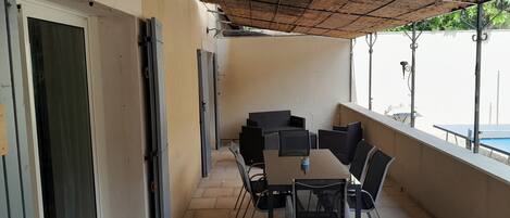 A covered outdoor seating area with a table and chairs, a door, and a view of a pool.