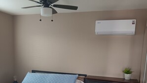 Een slaapkamer met een bed, een plafondventilator, een dressoir en een airconditioning.
