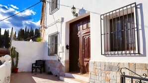 A white building with a wooden door and barred windows, a stone wall, and a cactus plant. - Casa Paradis - Callosa d'En Sarria, Costa Blanca (Callosa d'En Sarria)