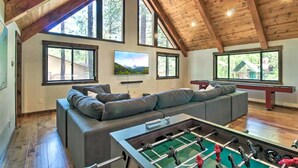 Een ruime loft met een hoge plafond, grote ramen, een grijze modulaire bank, een tafelvoetbalspel en een flatscreen televisie.