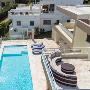 A rooftop pool area with lounge chairs and a sun lounger.